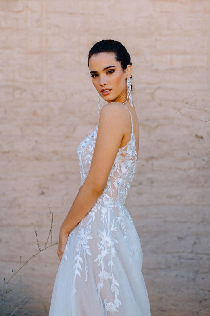 The Lexi gown features detachable off-shoulder straps and lace appliqués with glimmering pearl accents.